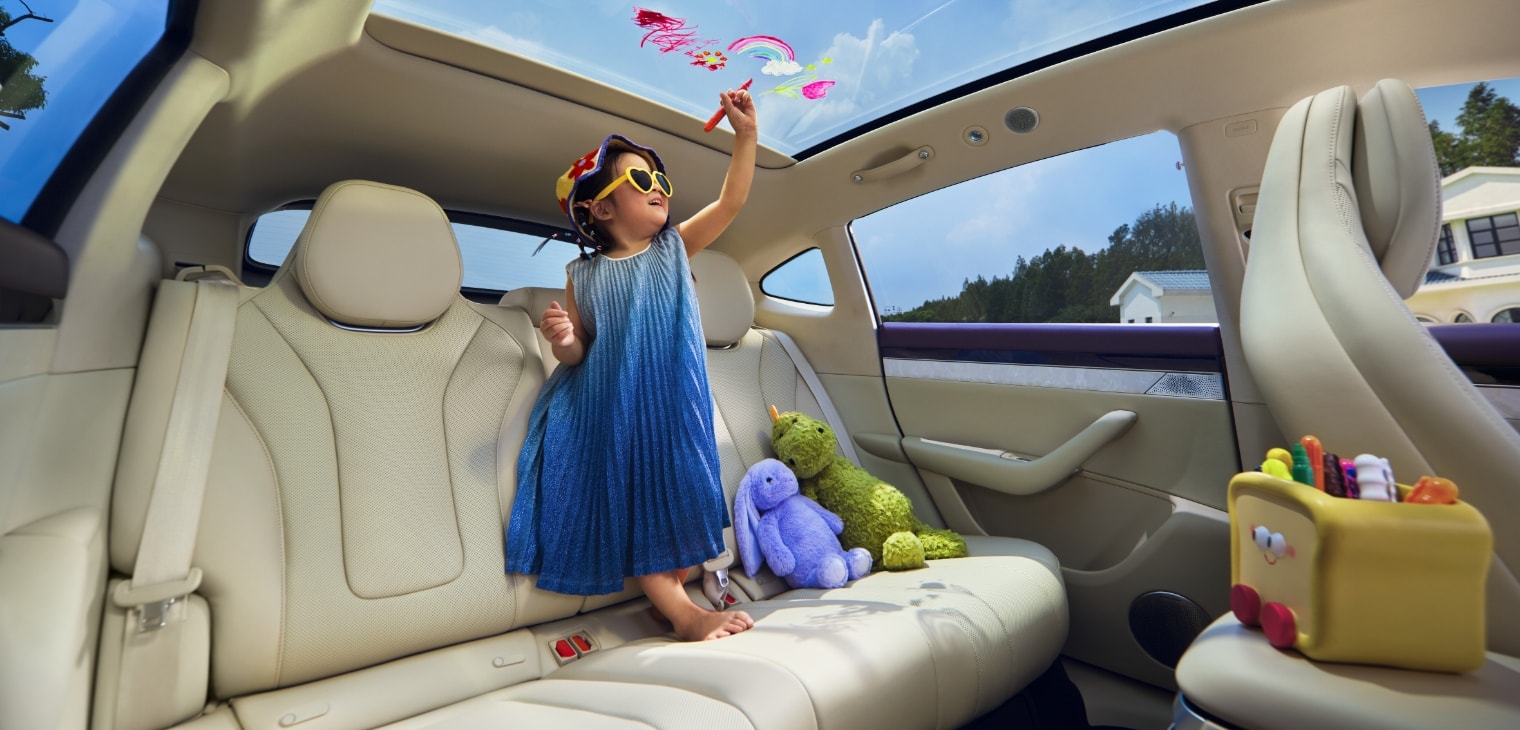 A young girl standing barefoot on the rear seat, doodling on the panoramic roof, showcasing the plush comfort of the Luxeed R7's Silk Cloud seats