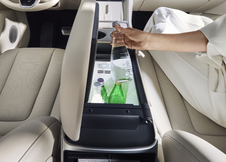 A woman opening the climate-controlled compartment from the front passenger seat and retrieving a beverage, showcasing the Luxeed R7's onboard climate-controlled storage function