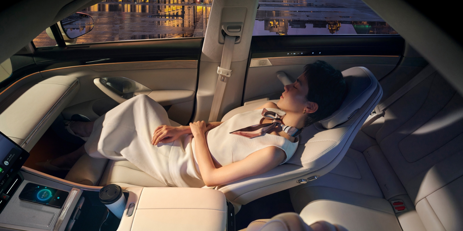 The user rests in the zero-gravity seat of the Luxeed New S7, demonstrating the seat's comfort